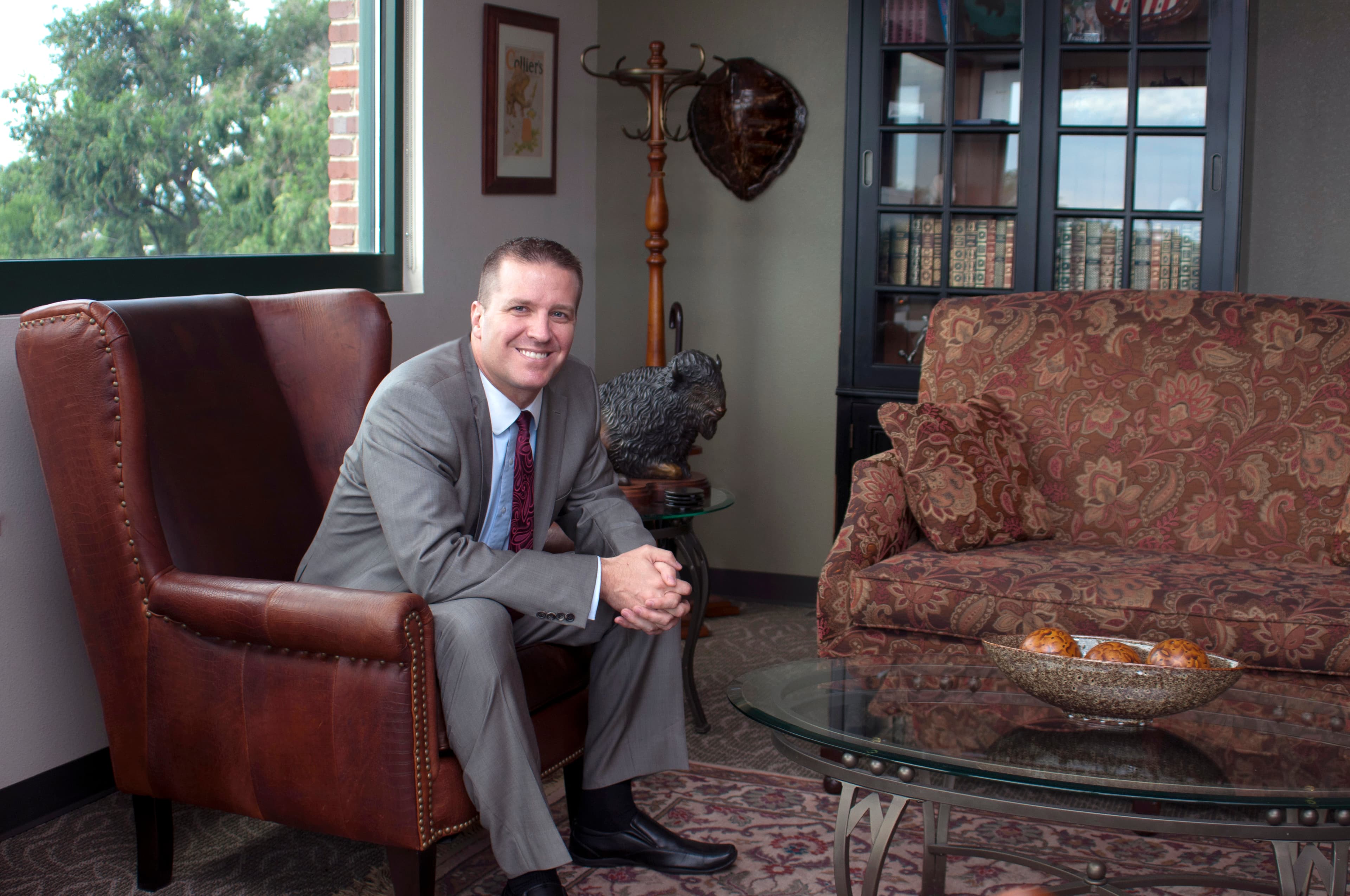 Brian J. Bagley seated in a leather wingback chair in the firm's office, a bookcase of law reports and a bronze bison behind him.
